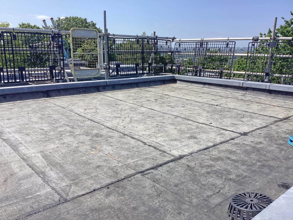 Close-up of worn flat roof prior to refurbishment, showing cracked felt and weathered finish.